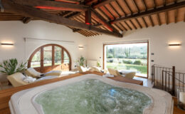 Luxurious indoor spa area featuring a jacuzzi, comfortable loungers, and large windows overlooking a scenic garden, with rustic wooden beams and warm lighting creating a relaxing atmosphere.