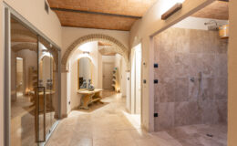 Luxurious bathroom interior featuring arched doorways, natural stone tiles, a spacious walk-in shower, and elegant lighting, designed for relaxation and comfort.
