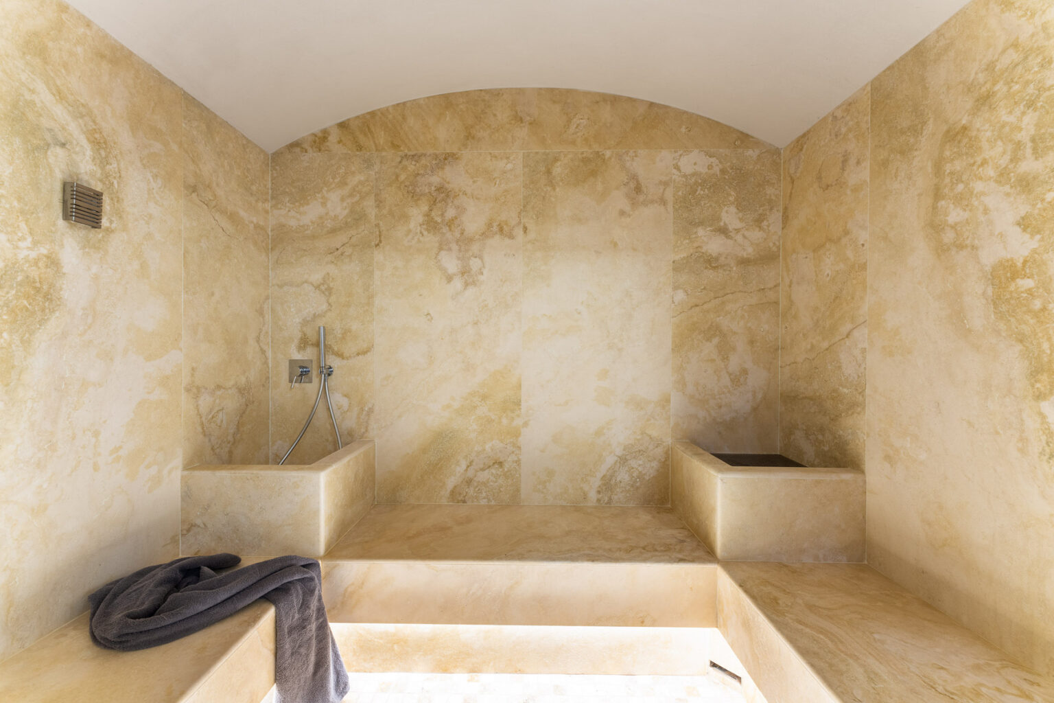 Luxurious bathroom interior featuring warm beige stone walls, a spacious shower area, and a modern faucet. Soft lighting enhances the elegant design, creating a serene atmosphere. | Only on SopranoVillas