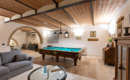 Spacious game room featuring a classic billiards table, cozy gray sofa, elegant wooden furniture, and stylish decor under a wooden beam ceiling, perfect for entertainment and relaxation.