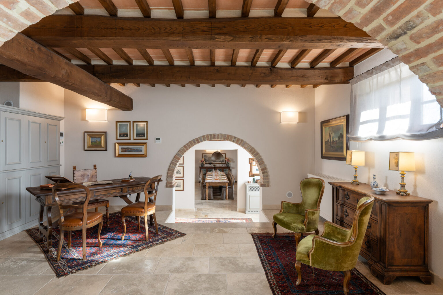 Cozy living room with wooden beams, vintage furniture, and a dining area featuring a wooden table and chairs, complemented by decorative artwork and warm lighting. | Only on SopranoVillas