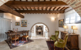 Cozy living room with wooden beams, vintage furniture, and a dining area featuring a wooden table and chairs, complemented by decorative artwork and warm lighting.