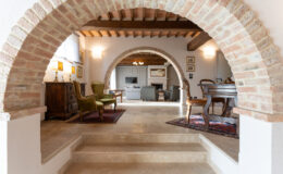 Interior view of a stylish living space featuring brick arches, wooden beams, and elegant furniture, showcasing a cozy and inviting atmosphere. The design blends modern comfort with classic architectural elements.
