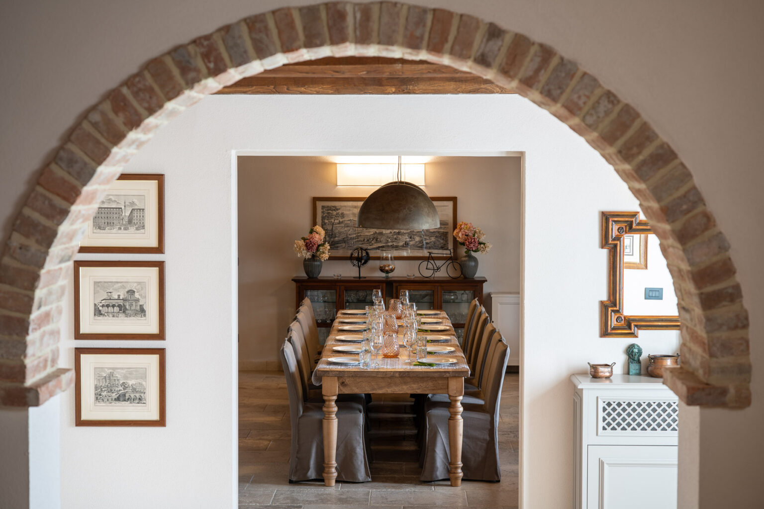 Interior view of a dining room featuring a rustic wooden table set for a meal, framed artworks on the walls, and a decorative archway leading into the space, creating a warm and inviting atmosphere. | Only on SopranoVillas
