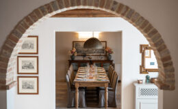 Interior view of a dining room featuring a rustic wooden table set for a meal, framed artworks on the walls, and a decorative archway leading into the space, creating a warm and inviting atmosphere.
