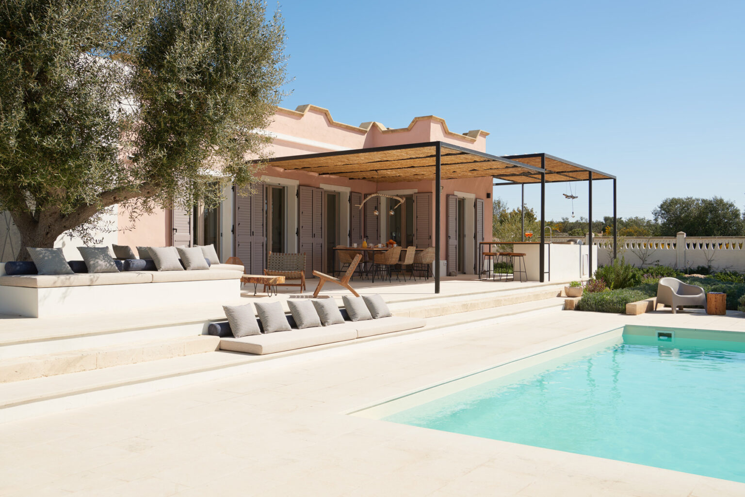 Modern villa with a swimming pool, featuring a spacious outdoor terrace and comfortable seating, surrounded by greenery under a clear blue sky. | Only on SopranoVillas