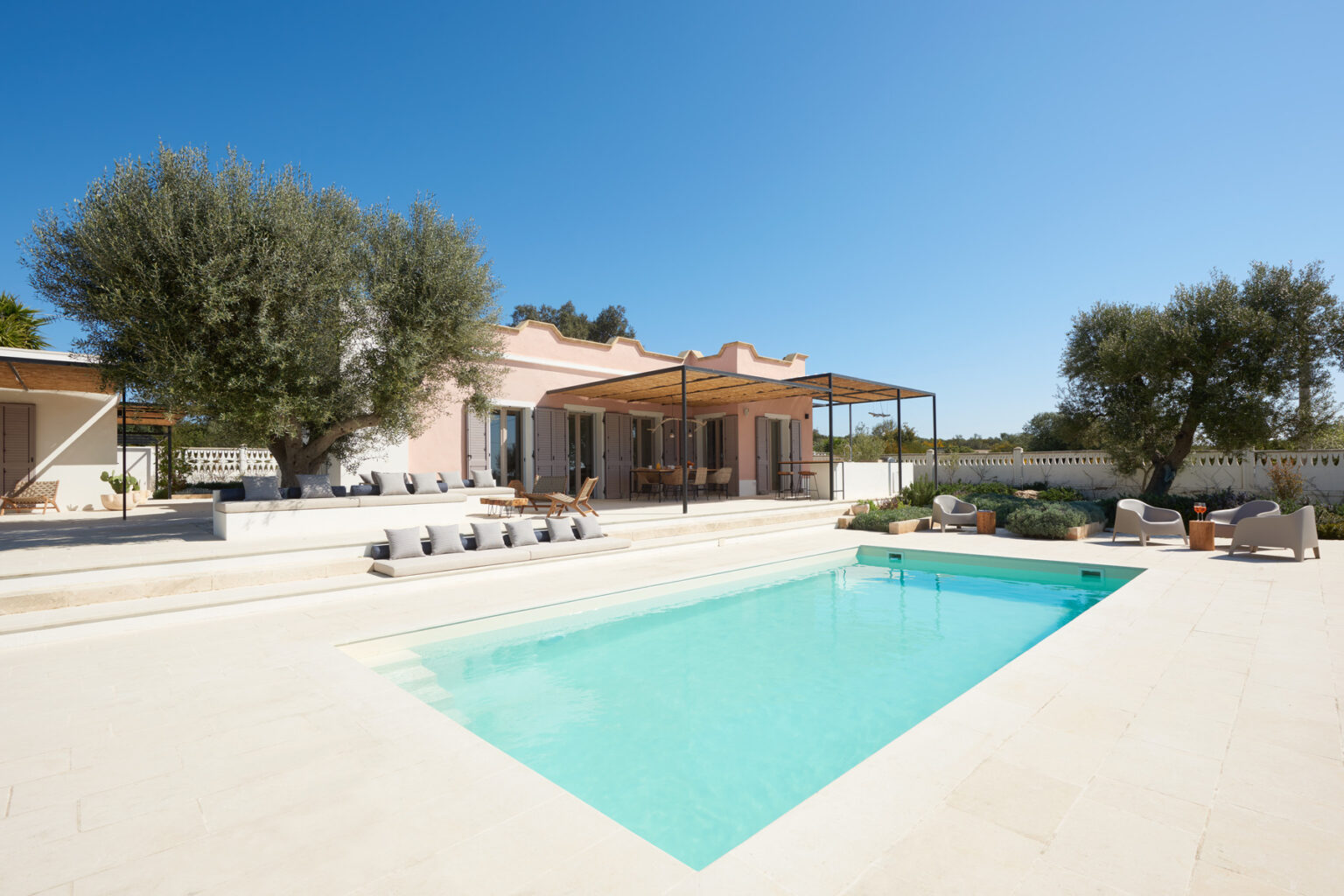 Modern villa with a swimming pool, surrounded by olive trees and outdoor seating, under a clear blue sky. Ideal for relaxation and outdoor living. | Only on SopranoVillas