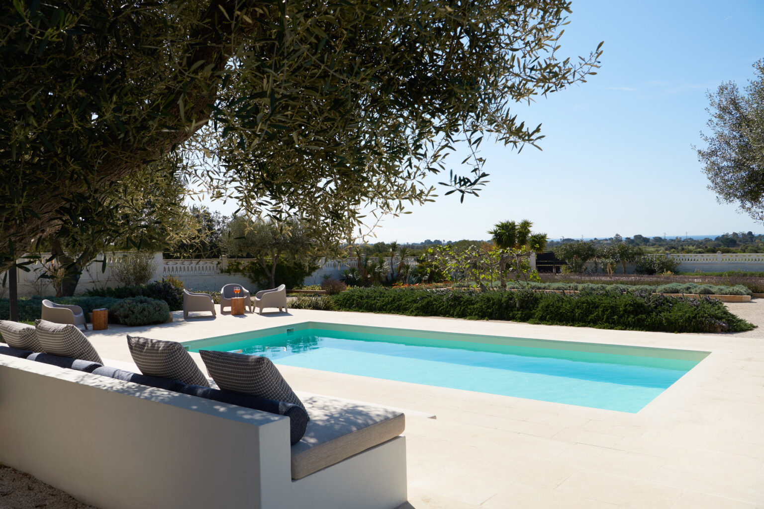 Serene outdoor pool area with olive trees, comfortable lounge chairs, and a scenic landscape in the background, perfect for relaxation and leisure. | Only on SopranoVillas