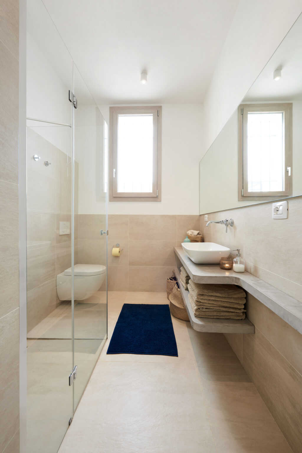 Modern bathroom with a glass shower enclosure, neutral stone walls, and a sleek countertop featuring a bowl sink. Soft towels are neatly stacked beside the sink, and natural light filters through large windows, creating a bright and airy atmosphere. | Only on SopranoVillas