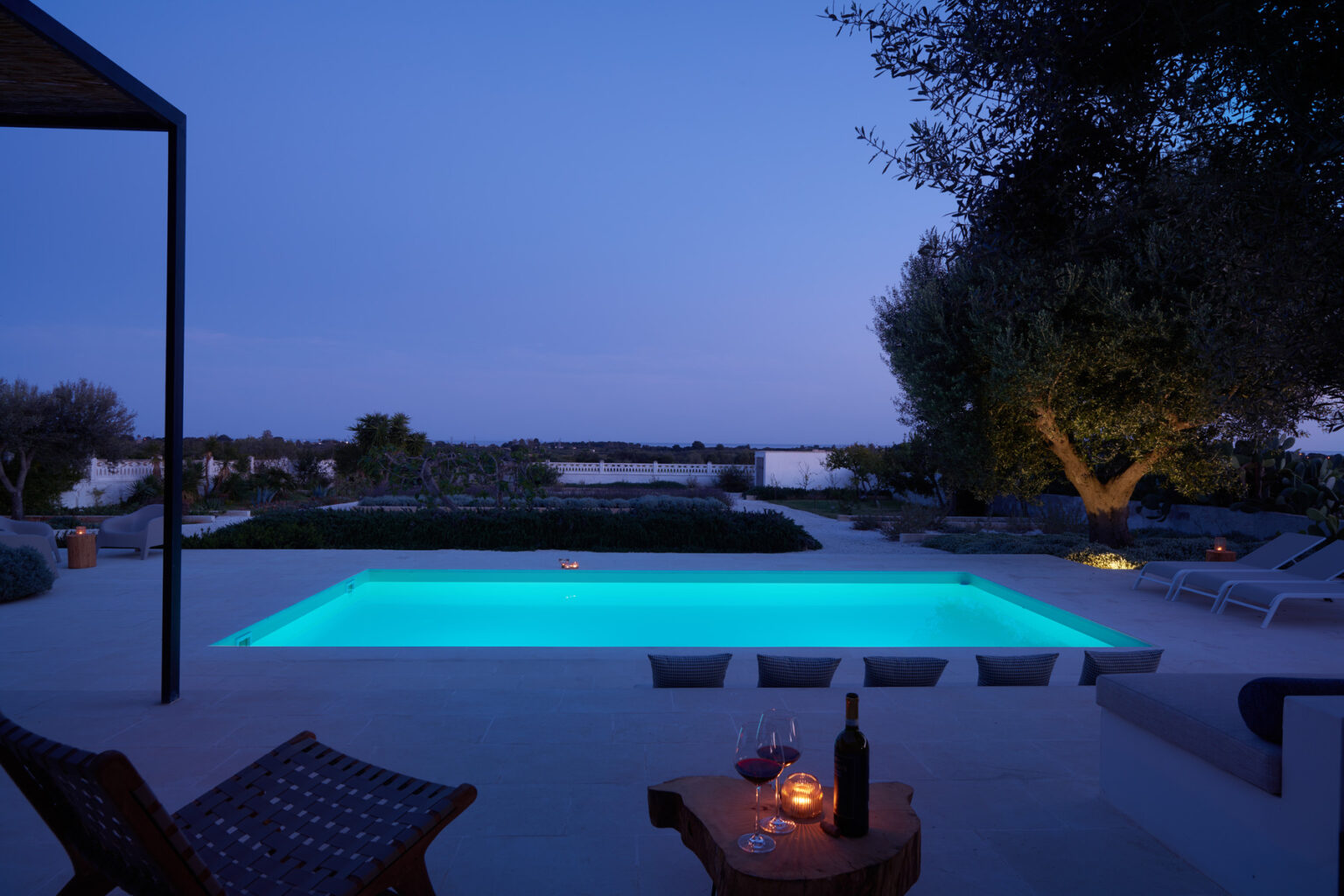 Modern outdoor pool illuminated at dusk, surrounded by stylish lounge chairs and a serene landscape, perfect for relaxation and evening gatherings. | Only on SopranoVillas
