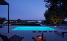Modern outdoor pool illuminated at dusk, surrounded by stylish lounge chairs and a serene landscape, perfect for relaxation and evening gatherings.