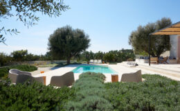 Modern outdoor pool surrounded by lush greenery and olive trees, featuring stylish seating and a relaxing atmosphere, perfect for leisure and entertainment.