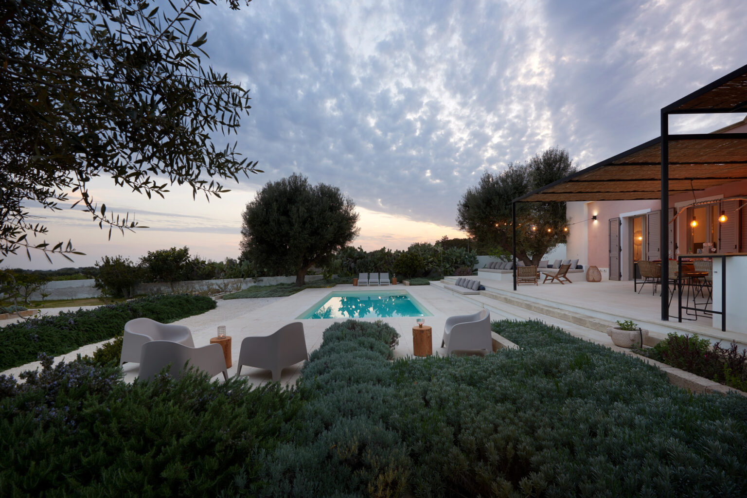 Modern villa with a pool surrounded by lush greenery and olive trees at dusk, showcasing a serene outdoor living space. | Only on SopranoVillas