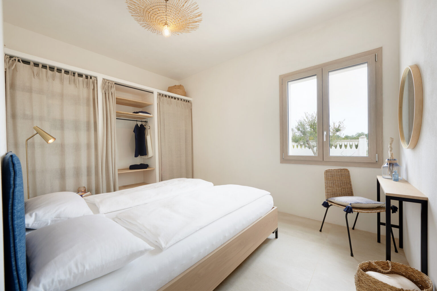 Modern bedroom with a double bed, natural light from a window, minimalist decor, a wooden chair, and a small desk, featuring a wardrobe with open shelving. | Only on SopranoVillas