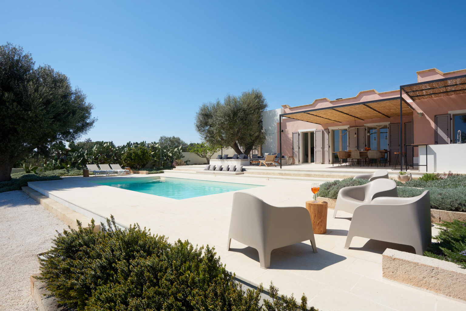 Modern villa with a swimming pool, surrounded by greenery and outdoor seating, set against a clear blue sky. Ideal for relaxation and leisure. | Only on SopranoVillas