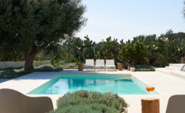 Modern outdoor pool surrounded by lush greenery and comfortable lounge chairs, perfect for relaxation in a sunny setting.