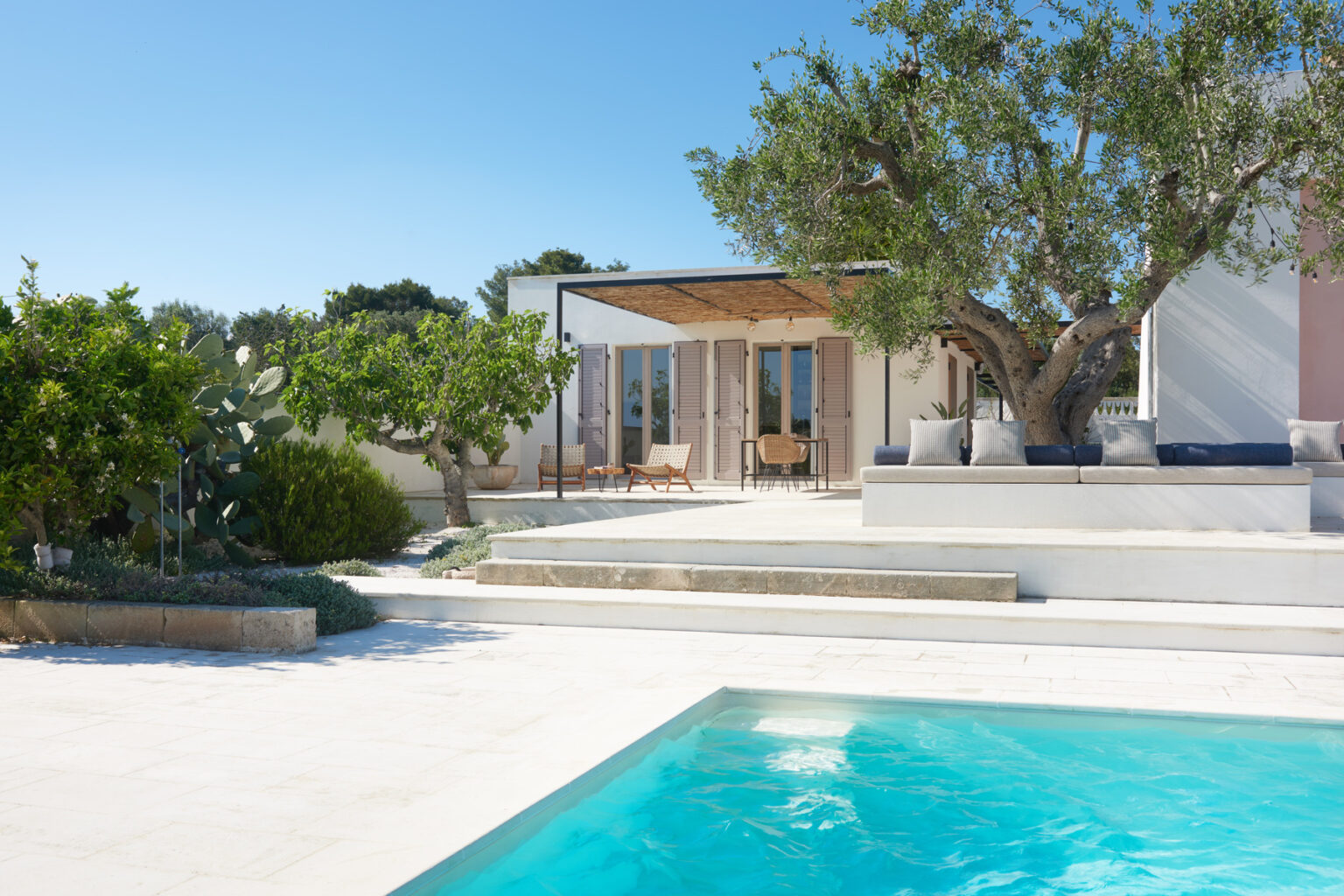 Modern villa with a swimming pool, surrounded by lush greenery and a sunny sky, featuring a spacious outdoor area and stylish architectural design. | Only on SopranoVillas