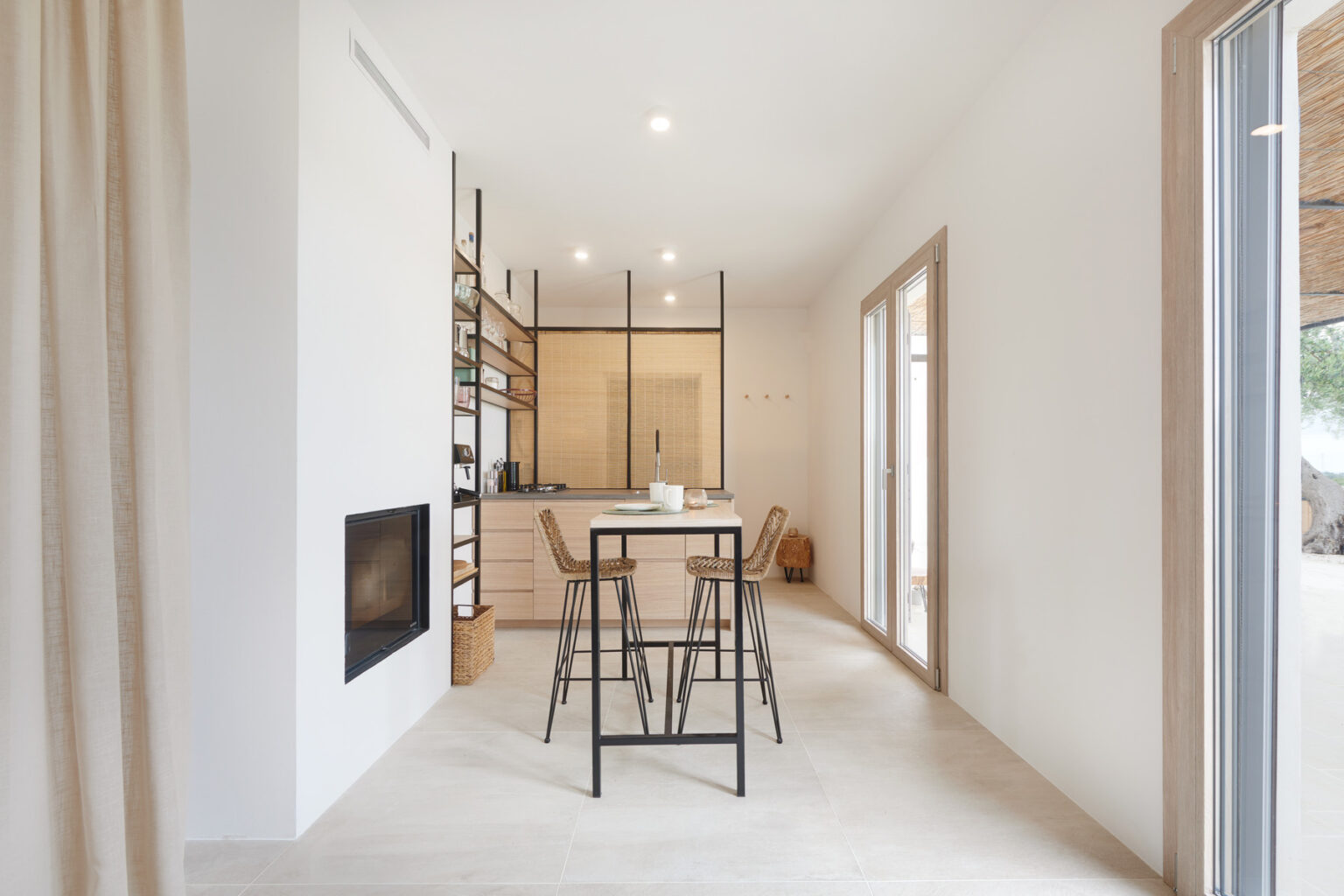 Modern minimalist kitchen and dining area featuring a sleek design with a small table and chairs, warm wood accents, and large windows allowing natural light to illuminate the space. | Only on SopranoVillas