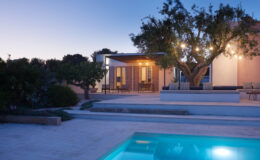 Modern villa with a swimming pool, surrounded by lush greenery, illuminated by soft evening lights, showcasing outdoor living space and contemporary architecture.