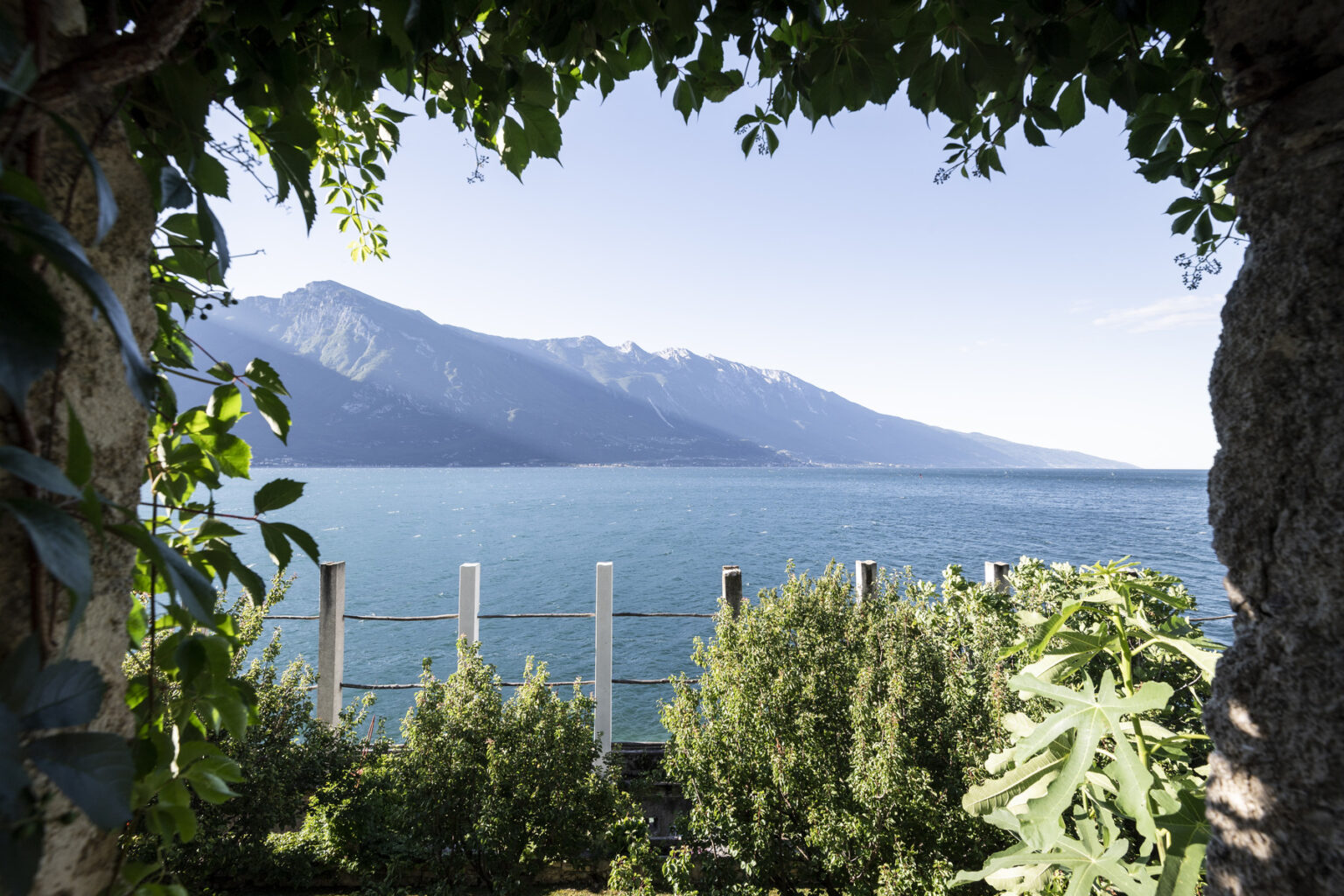Scenic view of a tranquil lake framed by lush greenery, with mountains in the background under a clear blue sky. Ideal for nature lovers and travel enthusiasts. | Only on SopranoVillas