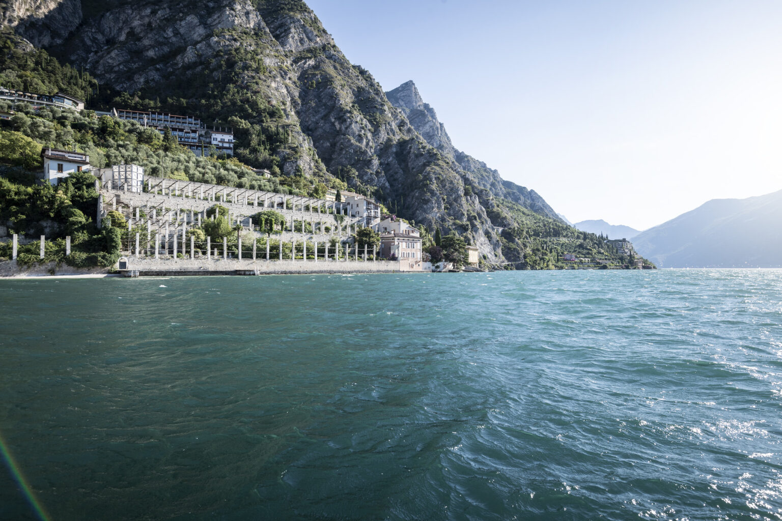 Scenic view of a lakeside resort with mountains in the background, showcasing clear blue water and lush greenery along the shoreline. | Only on SopranoVillas