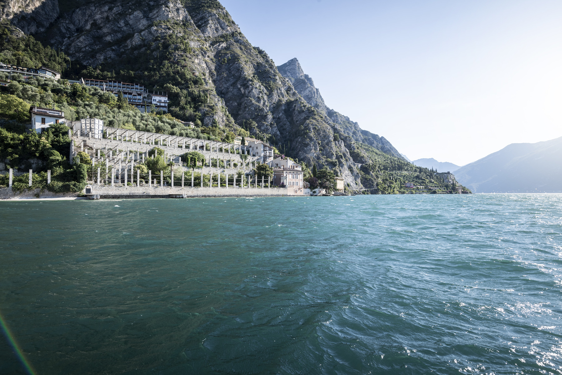 Scenic view of a lakeside resort with mountains in the background, showcasing clear blue water and lush greenery along the shoreline. | Only on SopranoVillas