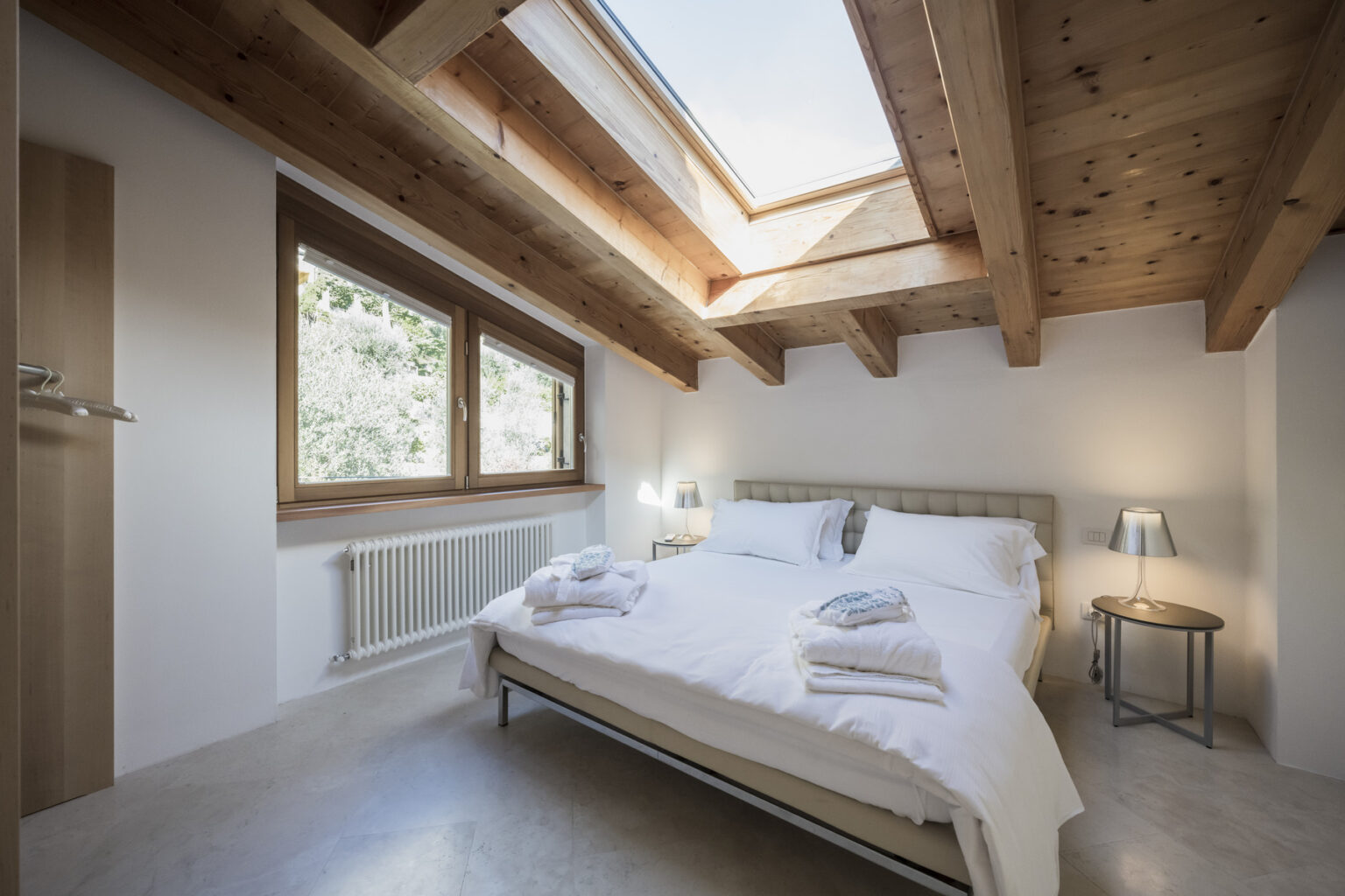 Modern bedroom with wooden beams, large windows, and a cozy double bed adorned with fresh towels, creating a bright and inviting atmosphere. | Only on SopranoVillas