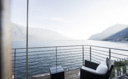Modern balcony overlooking a serene lake surrounded by mountains, featuring stylish outdoor furniture and a peaceful atmosphere.