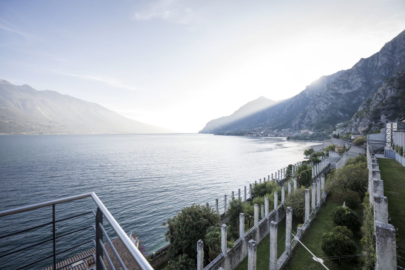 Scenic view of a tranquil lake surrounded by mountains, with a landscaped area in the foreground and a clear sky above. Ideal for travel and nature enthusiasts. | Only on SopranoVillas
