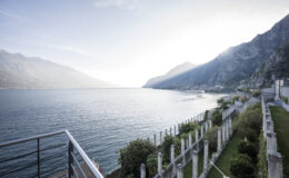 Scenic view of a tranquil lake surrounded by mountains, with a landscaped area in the foreground and a clear sky above. Ideal for travel and nature enthusiasts.