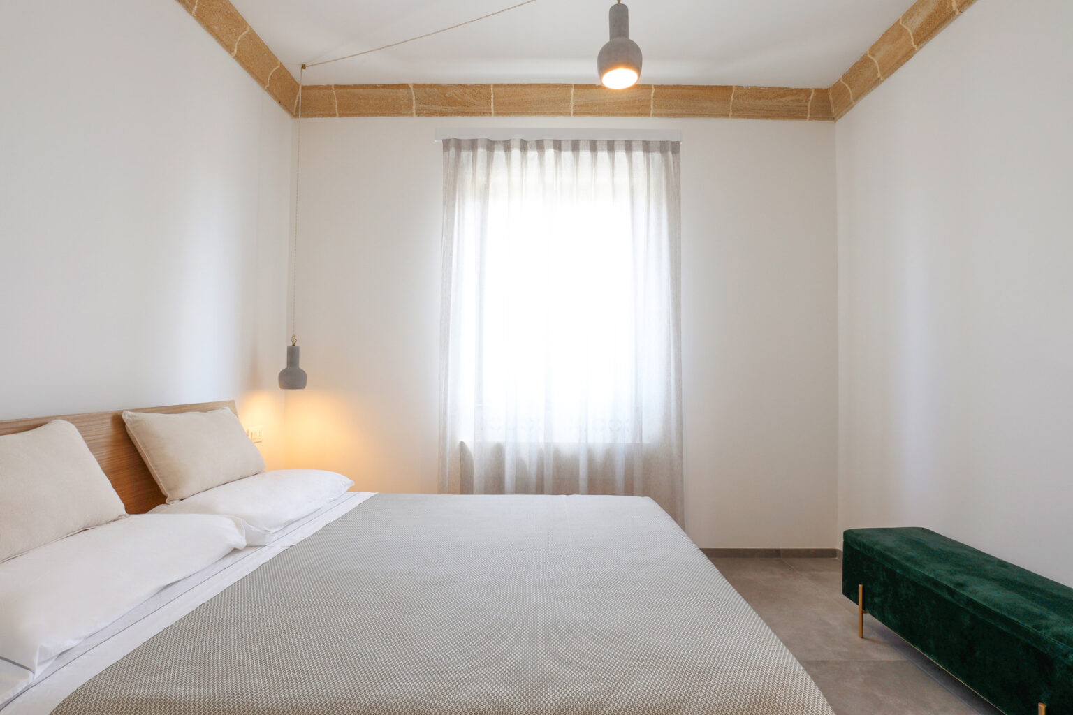 Modern bedroom interior featuring a neutral color palette, a cozy bed with light bedding, a large window with sheer curtains allowing natural light, and a stylish green bench accent piece. | Only on SopranoVillas
