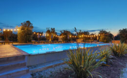 Serene outdoor swimming pool illuminated by string lights at dusk, surrounded by landscaped greenery and a peaceful atmosphere. Ideal for relaxation and evening gatherings.