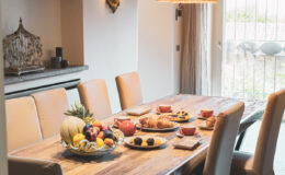 A beautifully arranged dining table featuring a variety of fresh fruits, pastries, and snacks, set in a modern dining room with natural light and stylish decor.