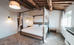 Cozy bedroom featuring a wooden four-poster bed with white bedding, rustic wooden ceiling beams, and warm lighting, creating a serene and inviting atmosphere.