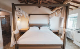 Elegant four-poster bed in a cozy room with wooden beams, featuring soft linens and bedside tables, perfect for a relaxing getaway.