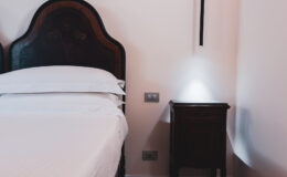 Cozy bedroom featuring a wooden headboard, neatly made bed with white linens, and a bedside table with a modern lamp. The soft lighting creates a warm and inviting atmosphere.