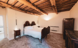 Cozy bedroom featuring a wooden beamed ceiling, a double bed with an elegant headboard, and vintage nightstands, creating a warm and inviting atmosphere.