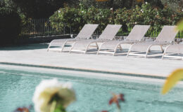 Lounge chairs by a serene swimming pool surrounded by lush greenery and blooming flowers, perfect for relaxation and outdoor leisure.