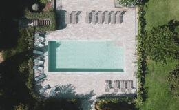 Aerial view of a modern swimming pool surrounded by lounge chairs and landscaped greenery, showcasing a serene outdoor relaxation area.