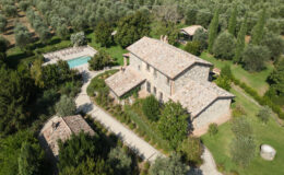 Aerial view of a rustic stone villa surrounded by lush greenery and olive trees, featuring a swimming pool and landscaped pathways. Ideal for a serene countryside retreat.