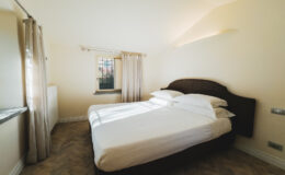 Cozy bedroom with a double bed, large windows, and soft natural lighting, featuring neutral-colored walls and elegant curtains. Ideal for relaxation and comfort.