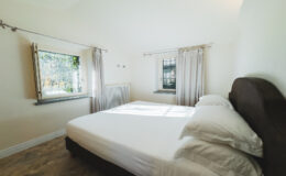 Bright and airy bedroom featuring a queen-sized bed with white linens, large windows with light curtains, and a cozy atmosphere, perfect for relaxation and comfort.
