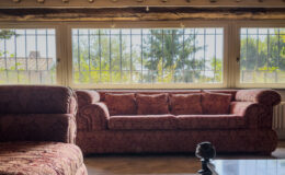 Cozy living room featuring a vintage red sofa, large windows with scenic views, and wooden ceiling beams, creating a warm and inviting atmosphere.