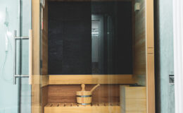 Modern wooden sauna with glass door and interior bench, featuring a traditional wooden sauna bucket and ladle, designed for relaxation and wellness.