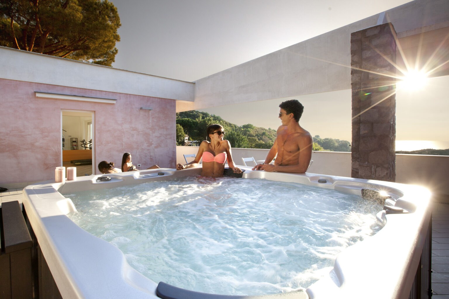 Couple relaxing in a hot tub on a rooftop terrace, with scenic views and sunlight illuminating the space, promoting a serene and luxurious getaway experience. | Only on SopranoVillas