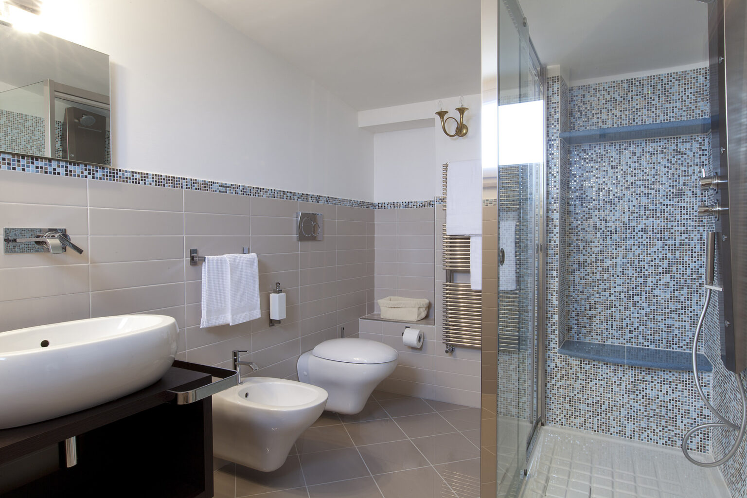 Modern bathroom featuring a sleek design with a glass shower, a large round sink, a toilet, and stylish tile accents. The space is well-lit with a mirror and decorative elements, creating a clean and inviting atmosphere. | Only on SopranoVillas