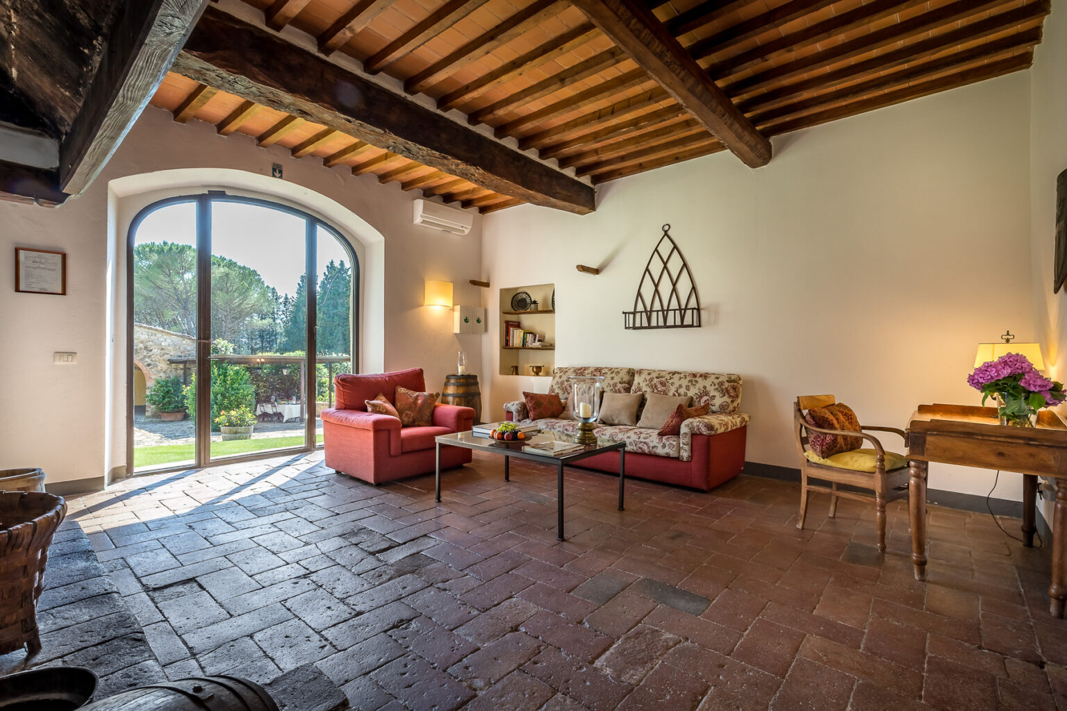 Cozy living room with rustic decor, featuring a comfortable seating area, wooden beams, and large windows opening to a garden view. Ideal for relaxation and enjoying natural light. | Only on SopranoVillas