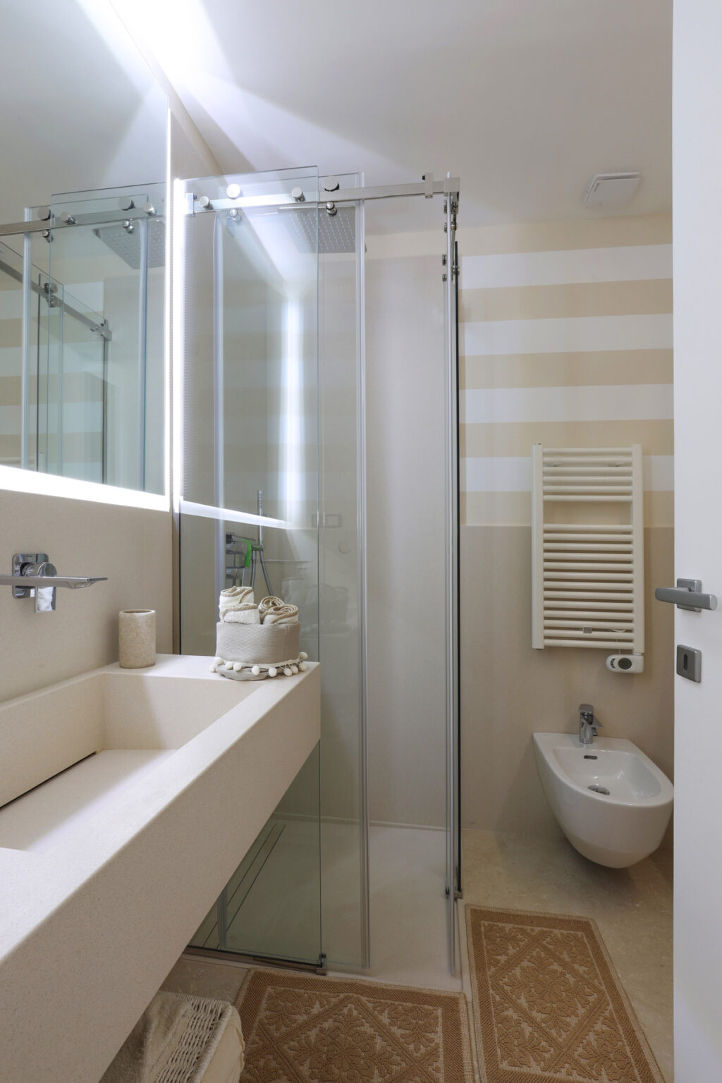 Modern bathroom interior featuring a glass shower, minimalist sink with decorative towel, and stylish striped wall design. | Only on SopranoVillas