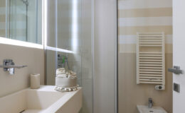 Modern bathroom interior featuring a glass shower, minimalist sink with decorative towel, and stylish striped wall design.