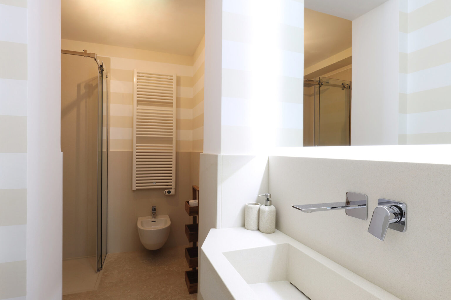 Modern bathroom featuring a sleek design with a walk-in shower, minimalist sink, and stylish fixtures. Light-colored walls with subtle stripes create a spacious feel, complemented by a towel radiator and contemporary accessories. | Only on SopranoVillas